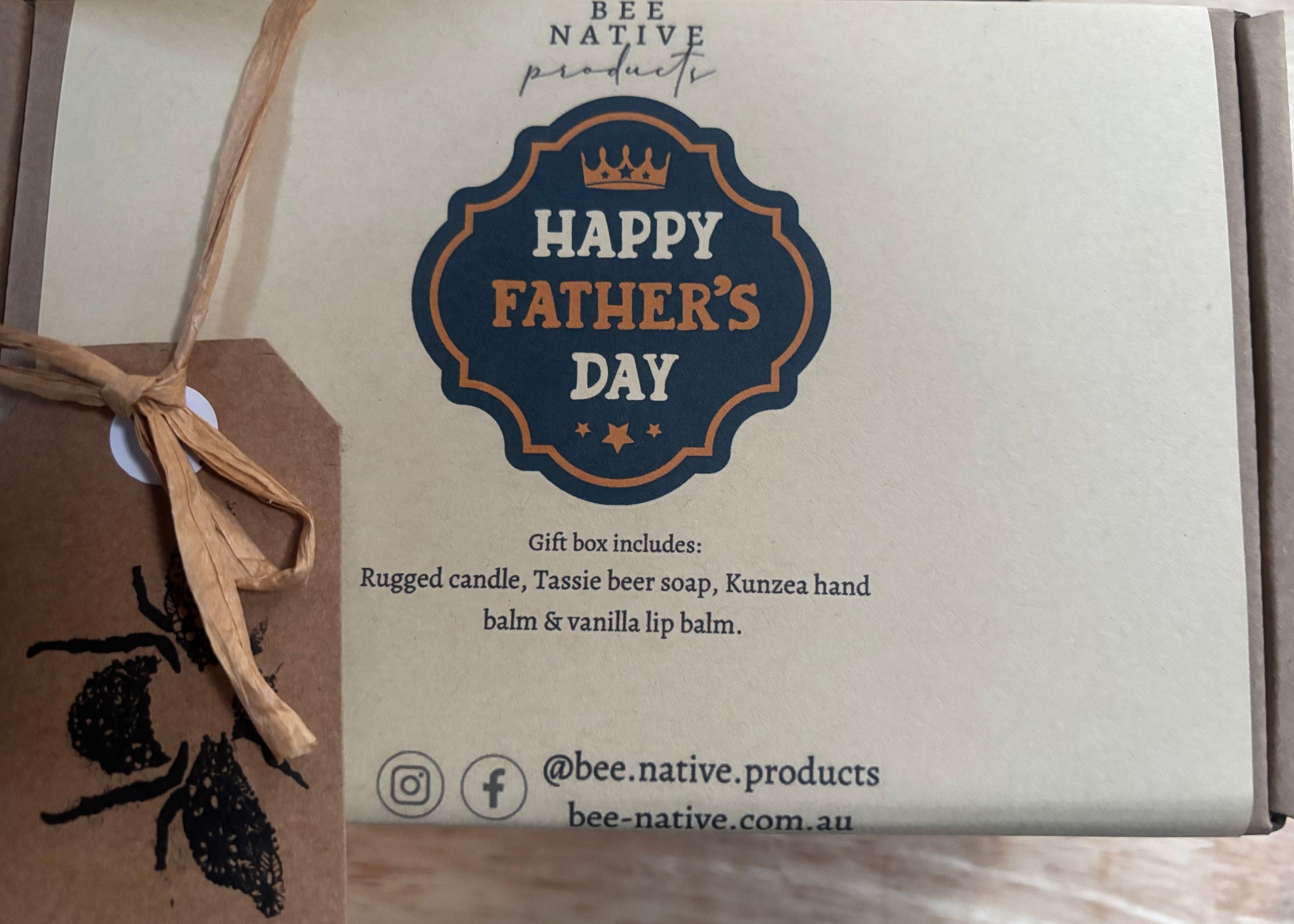 A Bee Native Products gift box for Father's Day, featuring a kraft paper insert with a blue and orange 'Happy Father's Day' emblem, a brown kraft paper tag with a black bee print tied with twine, and a cardboard outer box.