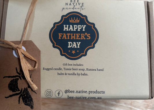 A Bee Native Products gift box for Father's Day, featuring a kraft paper insert with a blue and orange 'Happy Father's Day' emblem, a brown kraft paper tag with a black bee print tied with twine, and a cardboard outer box.